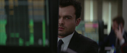 Alden Ehrenreich in a suit staring behind a desk looking lost.