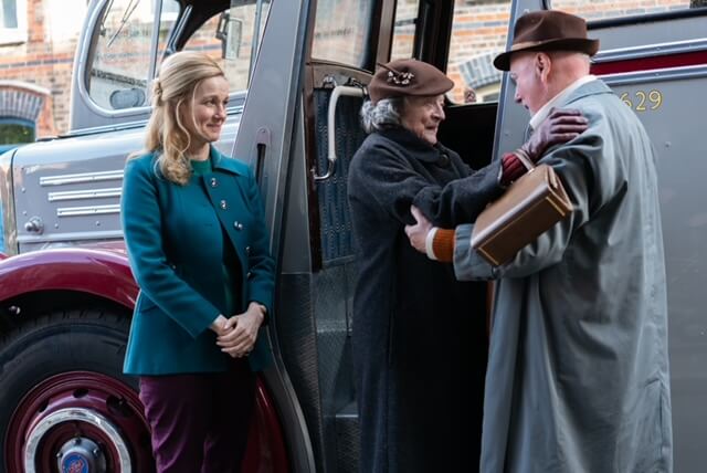 Two elderly people embracing outside near a truck with a young blonde woman looking on.