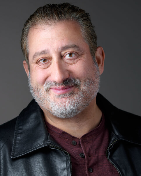 Actor Alfred Spielman smiling in a leather jacket.