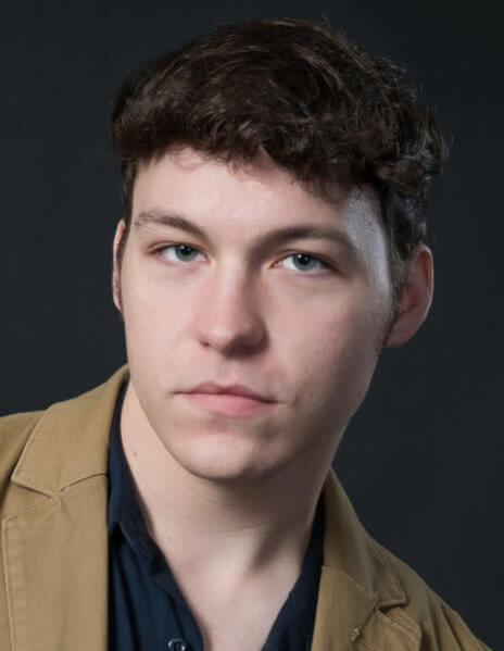 Actor Christopher Hudson in a tan jacket looking into the camera.