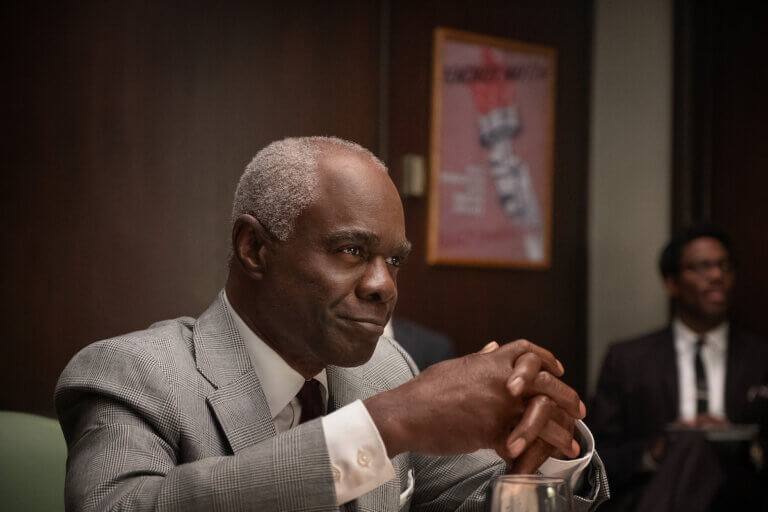 Glynn Turman sitting in a suit smiling.