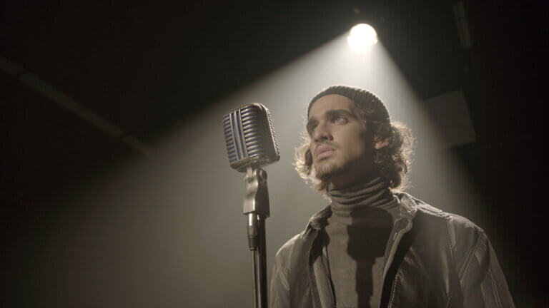 Hakim Brahimi in front of a microphone in a dark room for the film Montréal Girls.