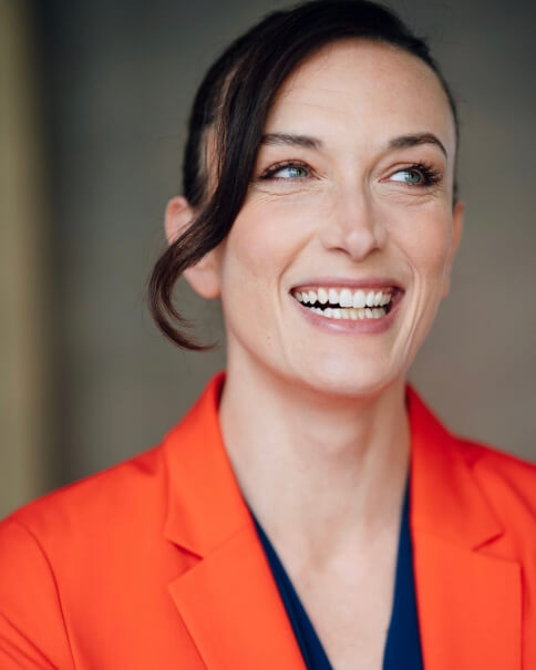 Actor Helena Geraci smiling in an orange shirt.