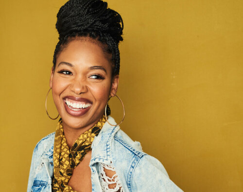 Actor Amber Ashley smiling and wearing a denim jacket over a with a yellow top.