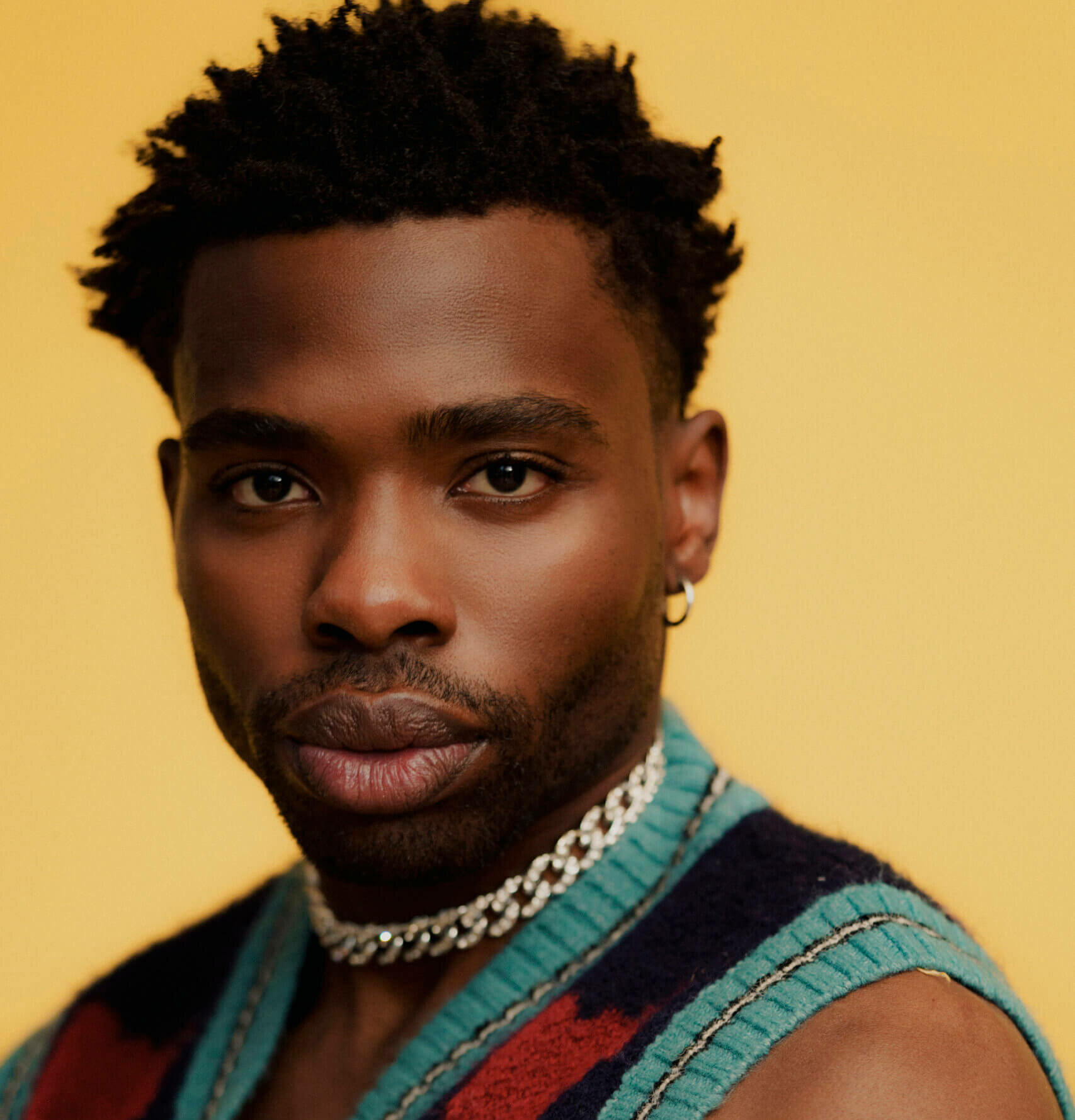 Actor John Adewumi wearing a sweater vest.