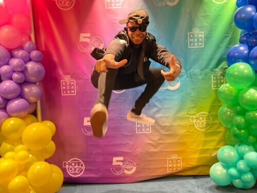 Actor J.Allyn Bivins doing a jump kick against a rainbow backdrop.