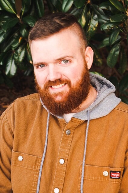 Actor James Wanek smiling outside in a brown denim jacket.