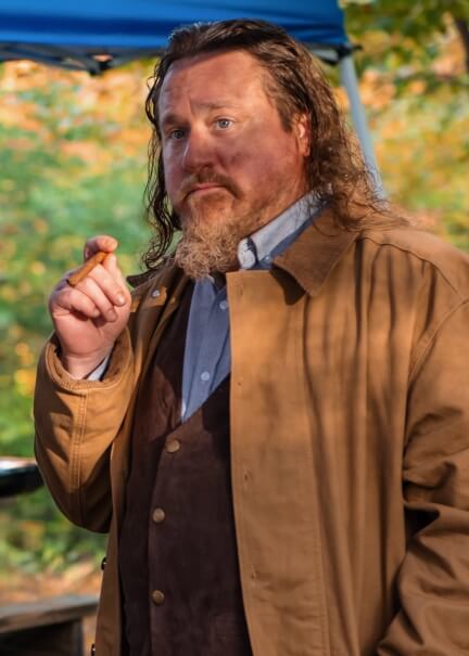 Actor John R. Smith Jr. in a brown trench coat smoking a cigar.