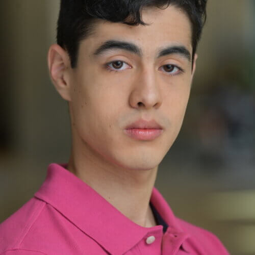 Actor Juan Rios looking serious in a pink shirt.