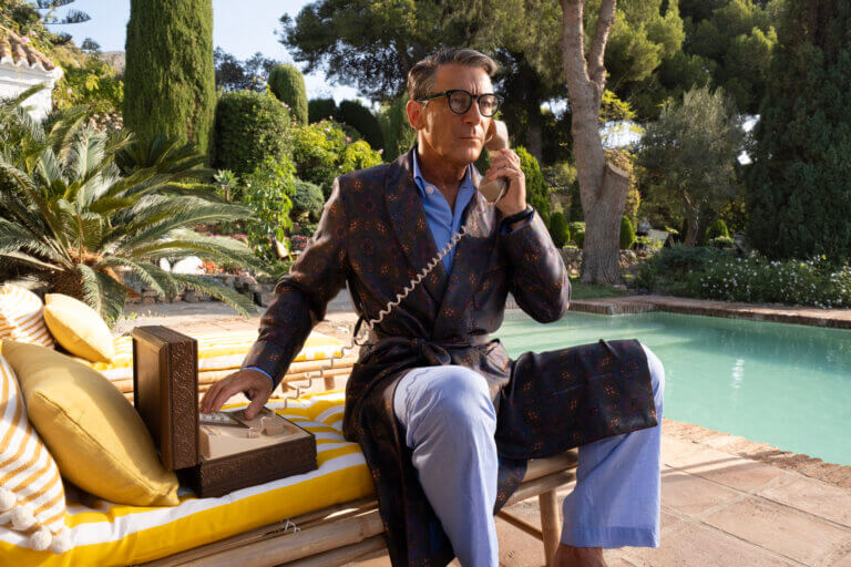 Jason Isaacs as Cary Grant on the phone in a bathrobe by the pool.