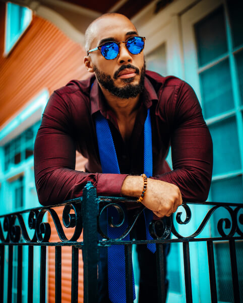 Rio Rocket in a red shirt and blue sunglasses looking over a balcony.