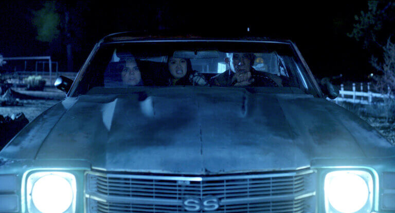 Two nervous woman and a shocked older man driving a car at night.