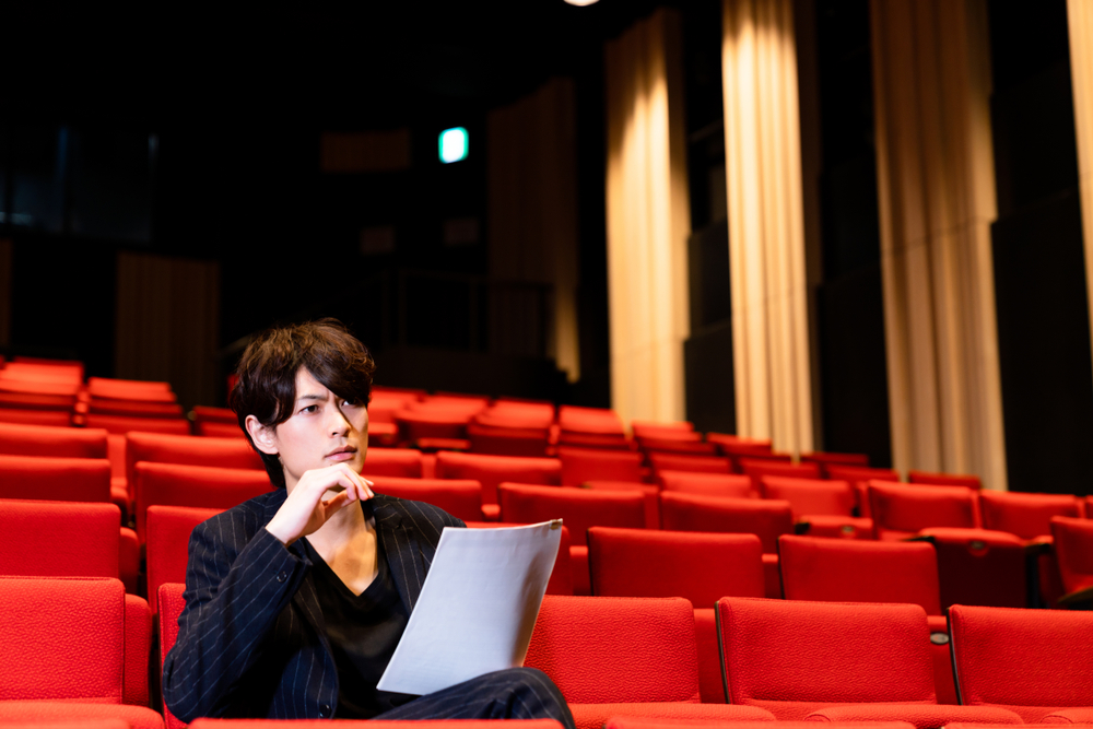 A casting director sitting in a seat watching a play, taking notes.