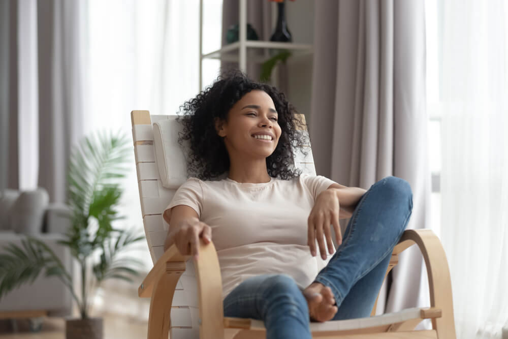 A calm and happy young African American woman relaxing at home in a cozy chair.