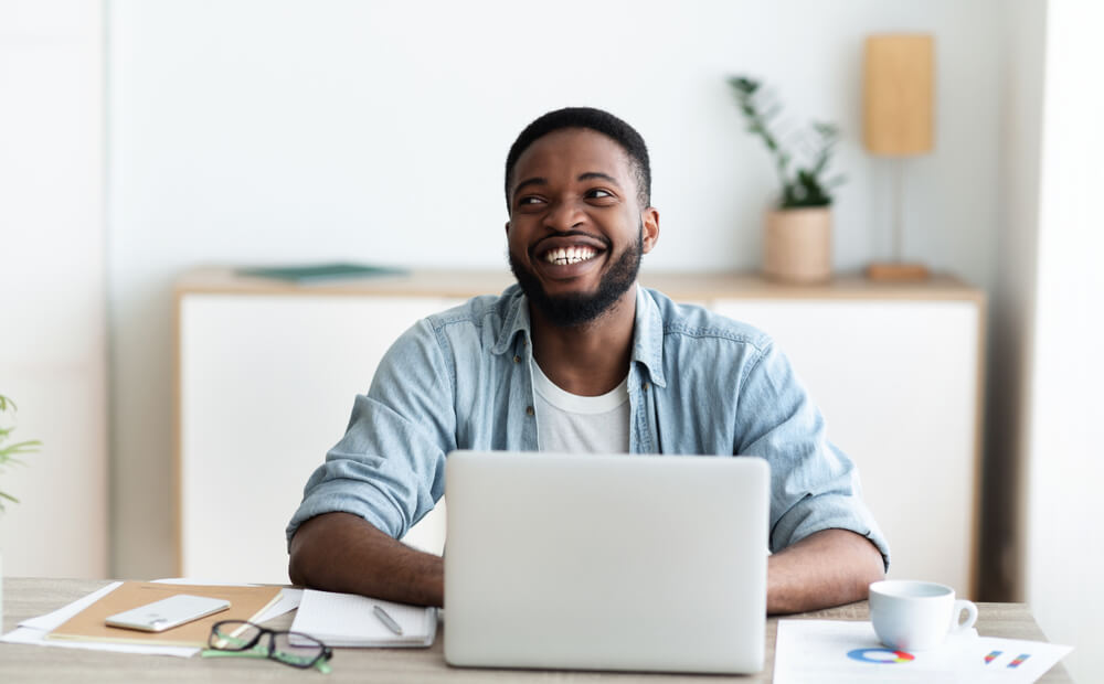 An actor smiling on his laptop with financial papers for his savings account on his desk.