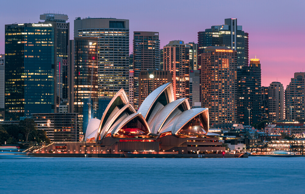 Sydney Opera house at dusk with the Sydney skyline in the background.