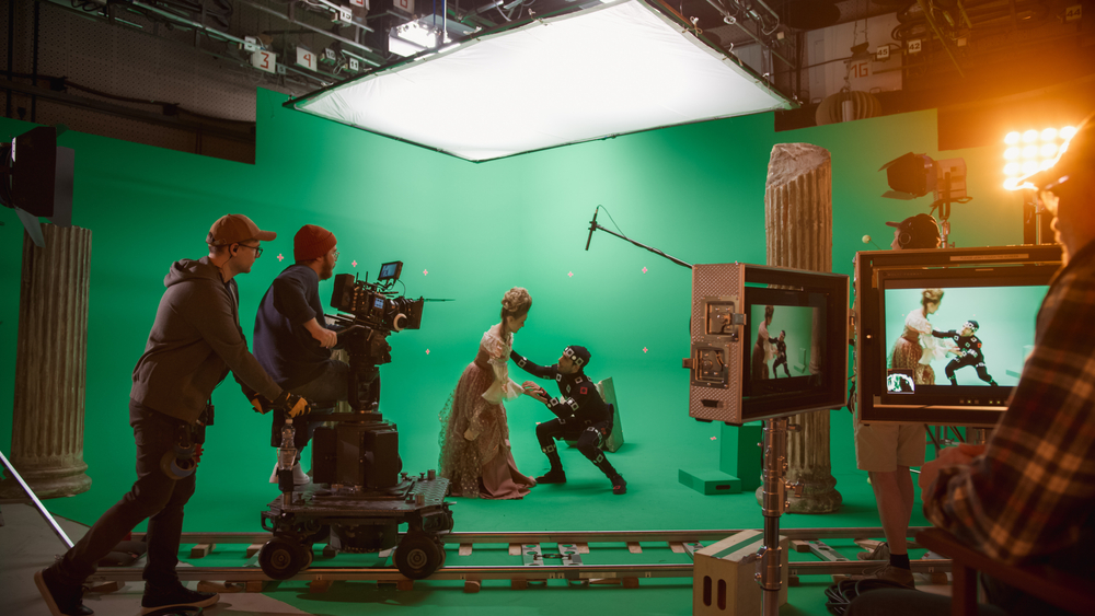 A film crew and actors shooting a scene with two actors on a green screen set.