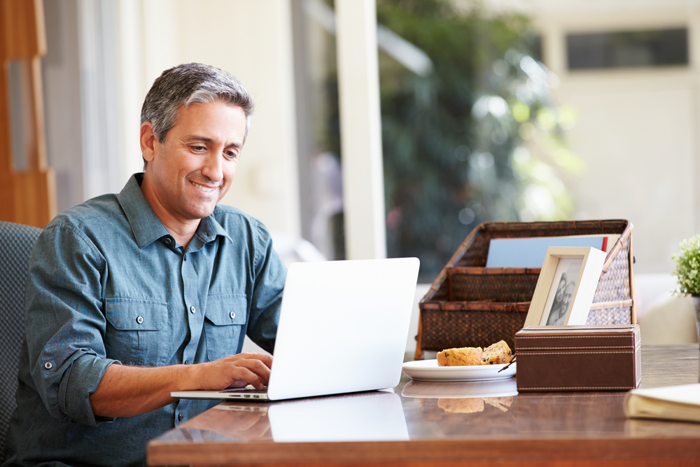 Middle aged hispanic man on his laptop smiling.