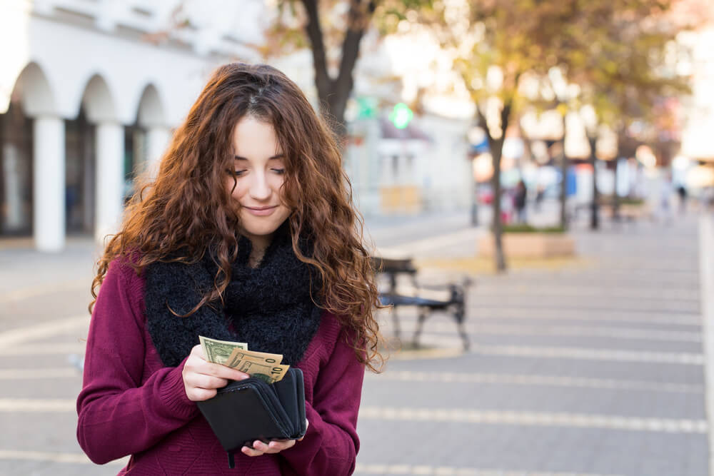 A young woman in the park putting money into her wallet.