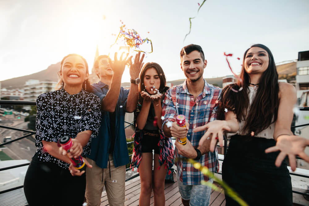 A group of diverse friends celebrating outside with confetti.