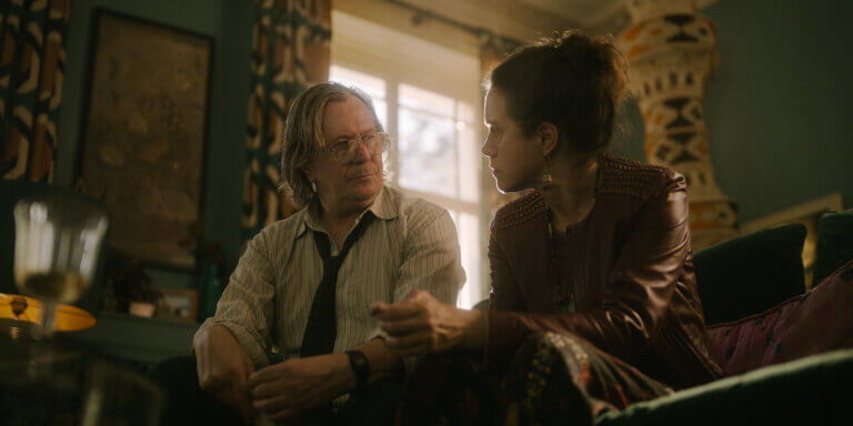 Actors Gary Oldman and Emily Bruni sitting on a couch in "Slow Horses,"