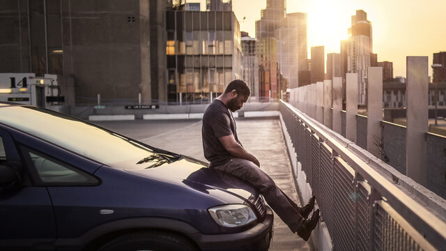 David Oyelowo sitting on his car hood looking upset.