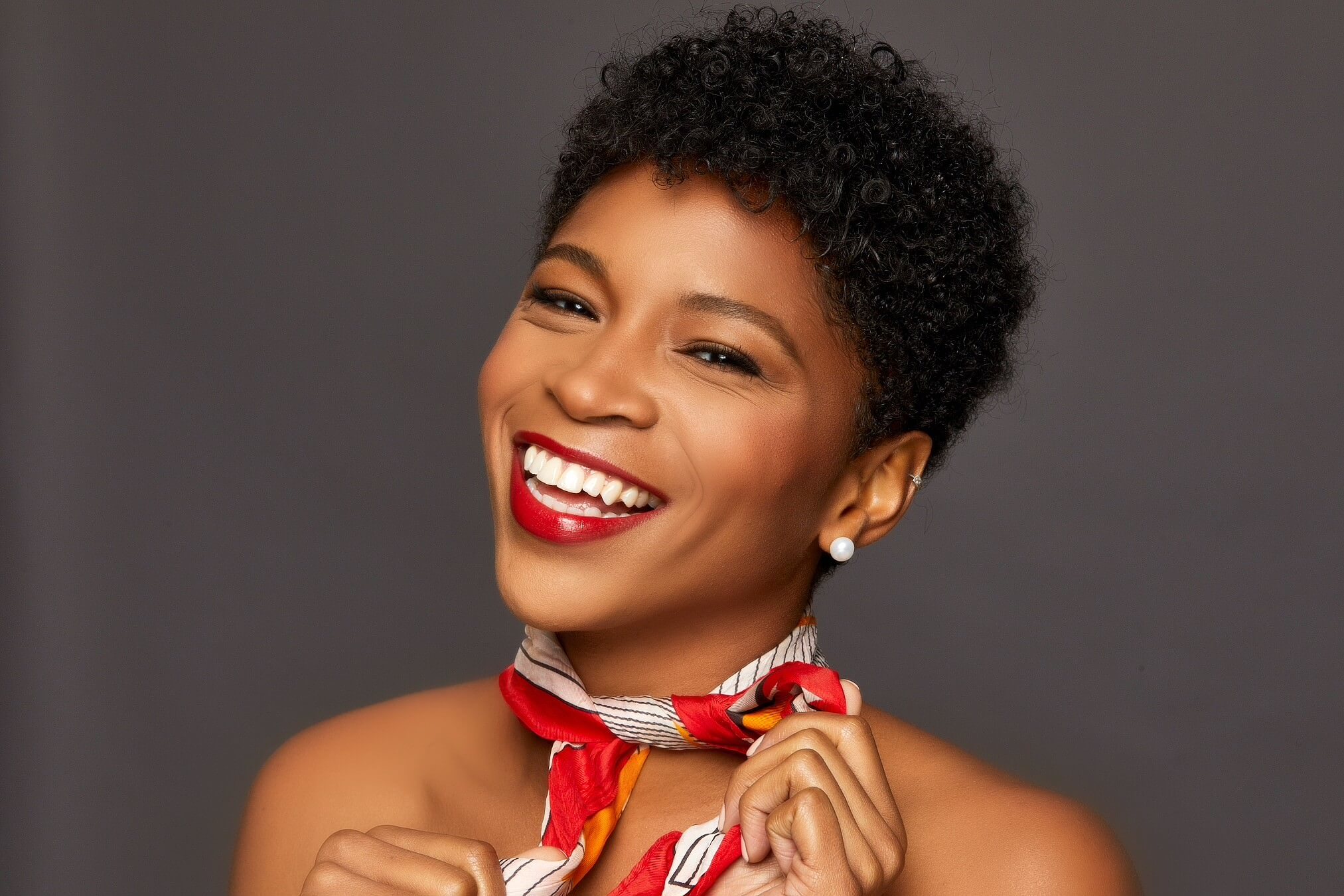 Actor Unissa Cruse touching an orange and white scarf smiling.