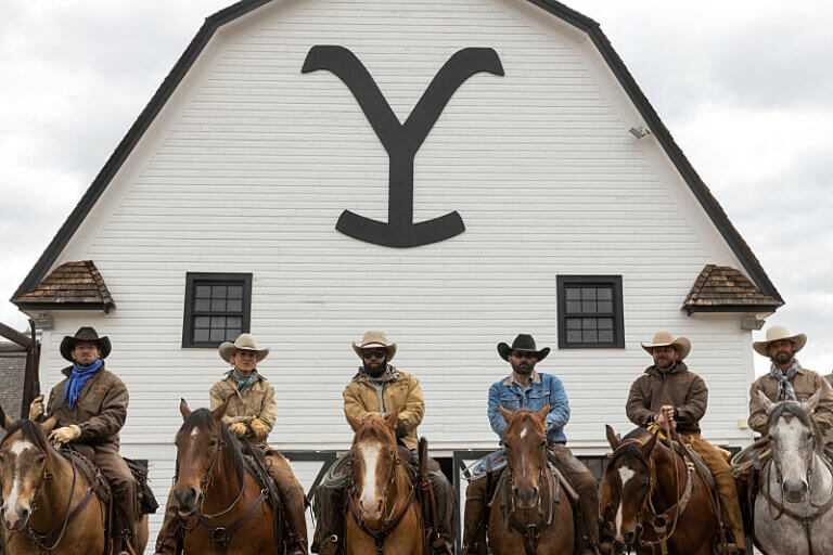 A group of cowboys on horseback in front of a building. Still from the show Yellowstone.