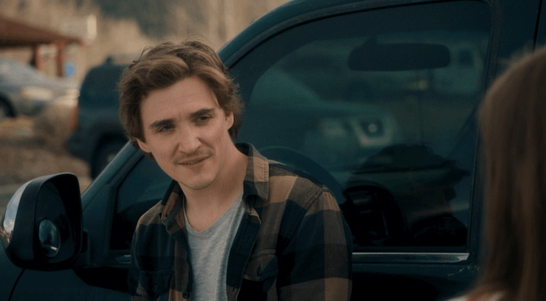 Actor Kyle Gallner in a flannel shirt outside by a car.