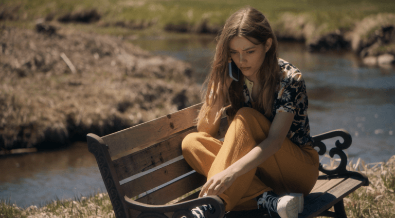 Grace Van Dien sitting on a park bench outside talking on the phone.