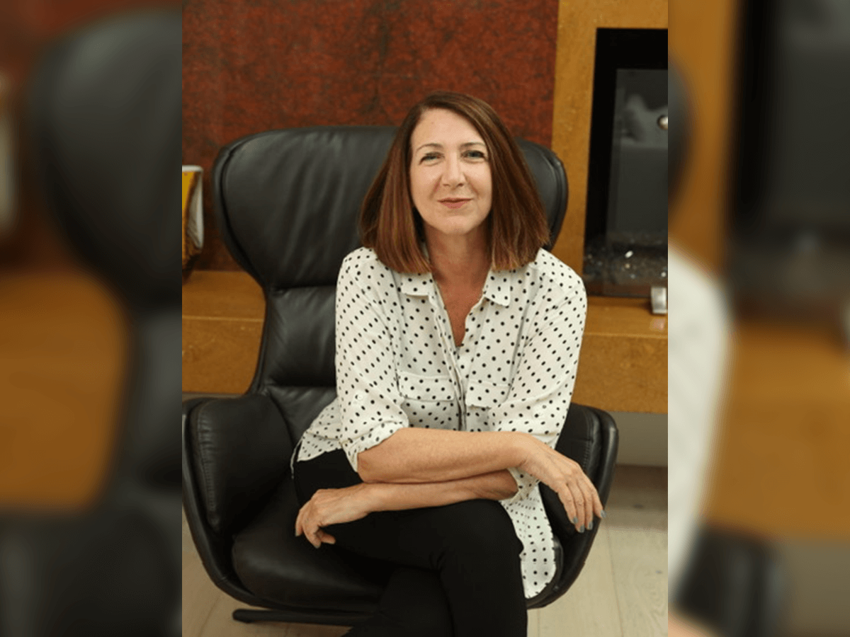 Nancy Nayor smiling and sitting in a chair inside.