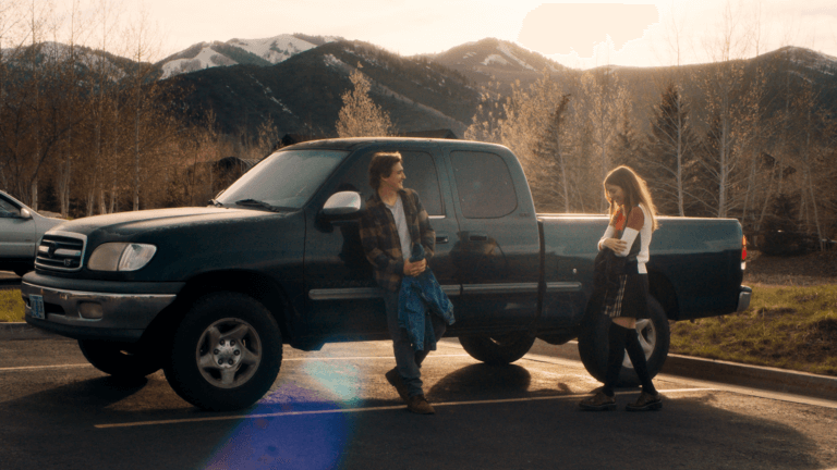 Actors Kyle Gallner and Grace Van Dien talking in front of a car.